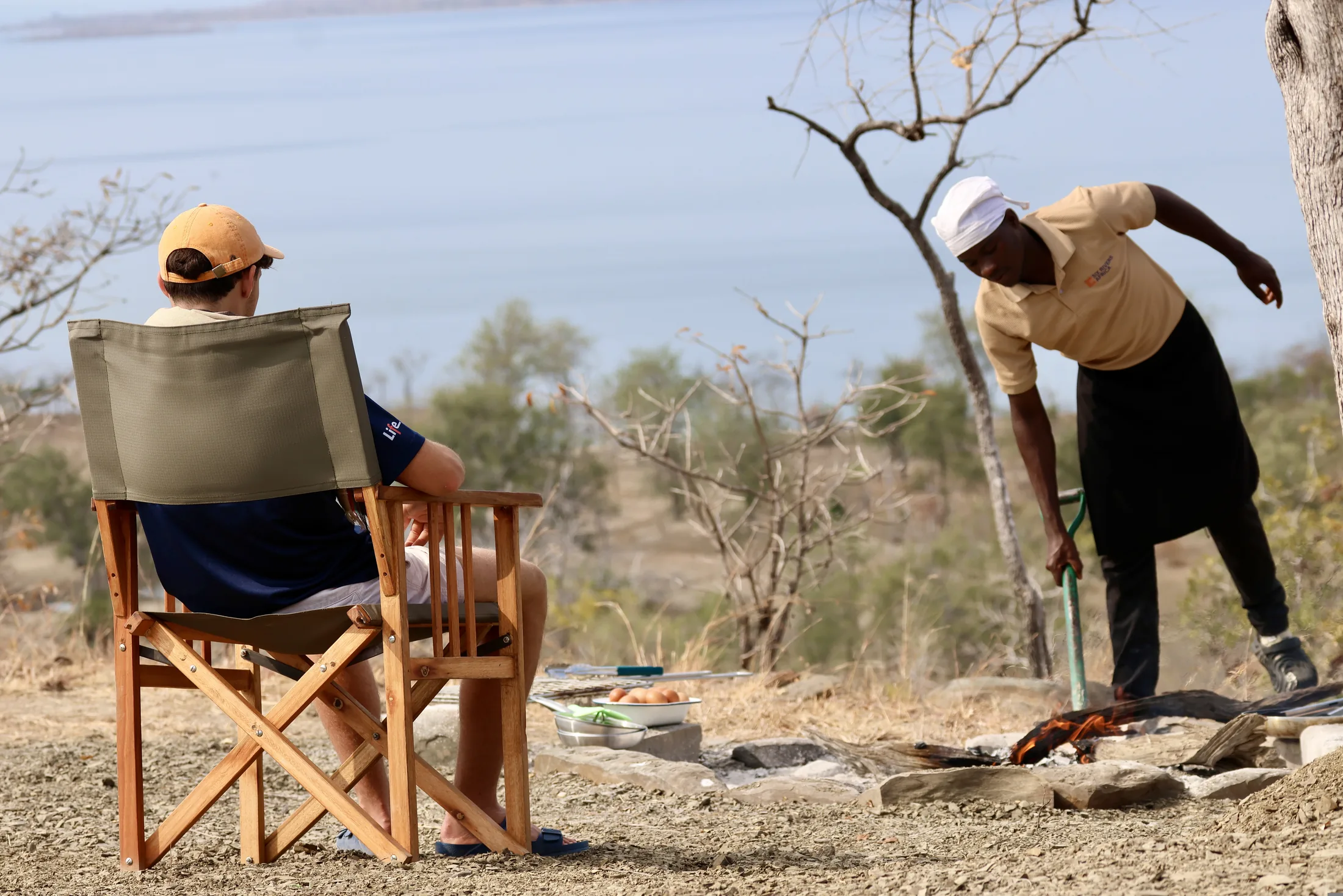 A guest seated by the Shangaa shoreline as camp staff prepare a fire